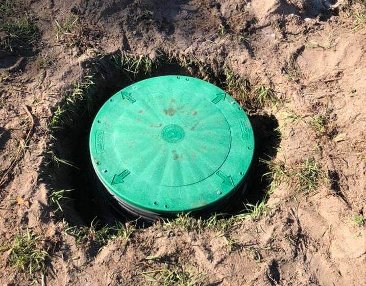 A green cover sits on top of a septic hole in the ground.