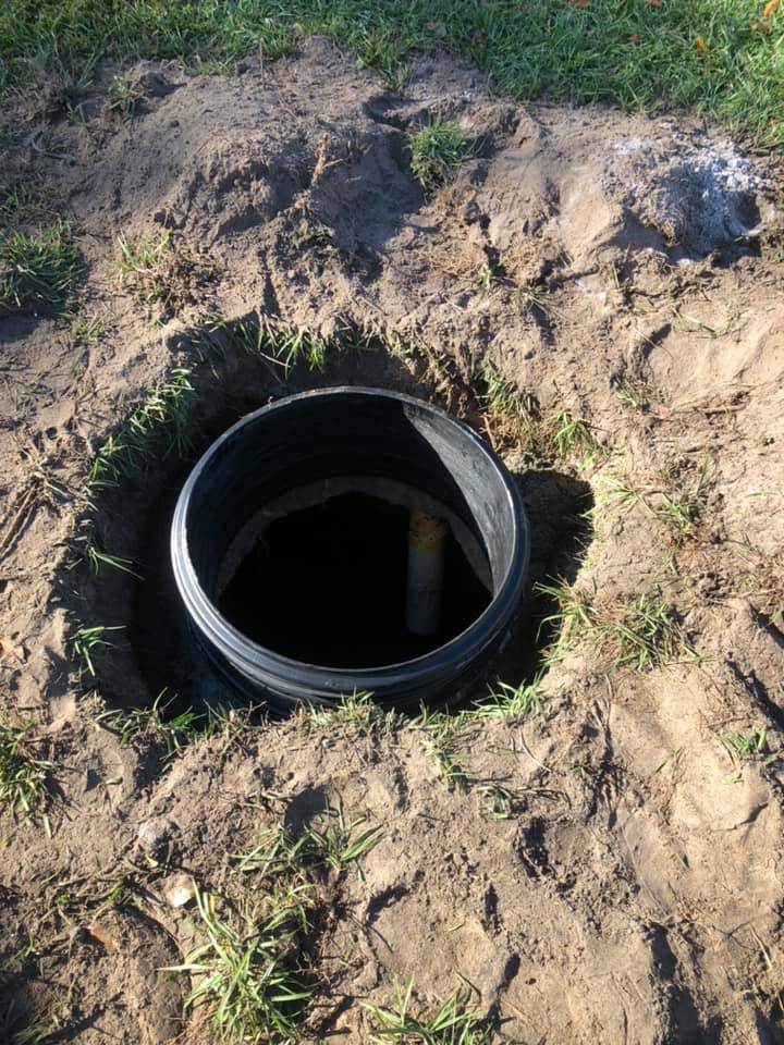 A grassy area with a black hole, possibly connected to Victor Plumbing or Septic services.