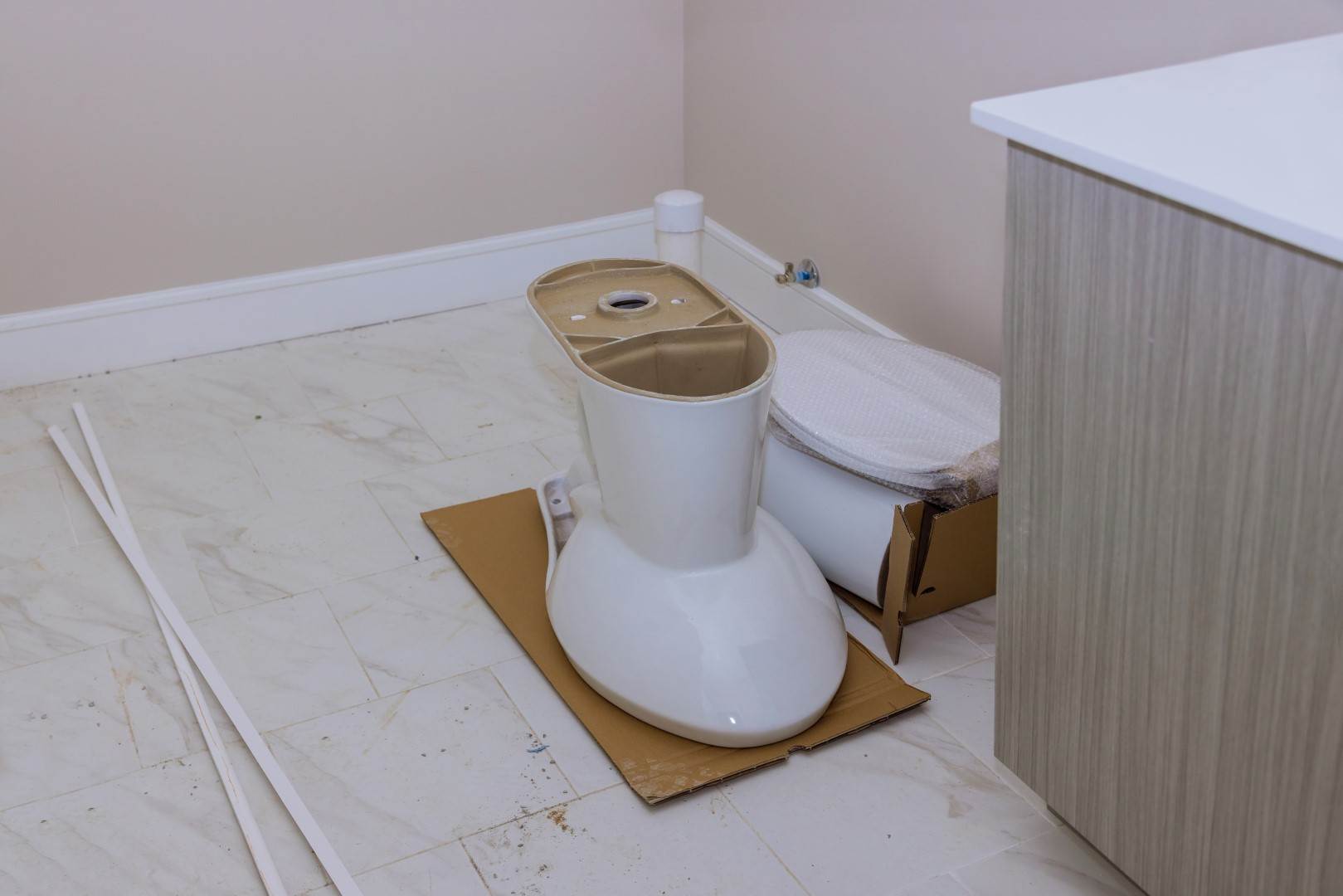 A white toilet sitting on a box in a bathroom, installed by Victor Plumbing.